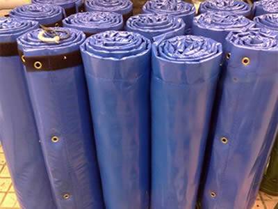 Many blue flexible sound barriers are packaged into rolls by plastic ropes on the ground.