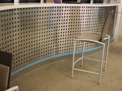 There is a chair in front of the perforated metal infill panel.