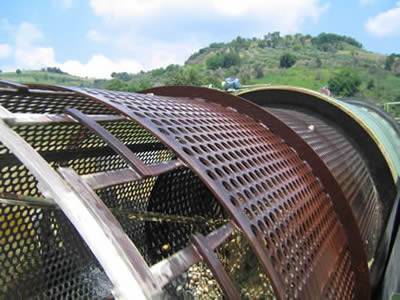 There is a cylindrical perforated vibrating screen in front a mount and many stones are in the screen.