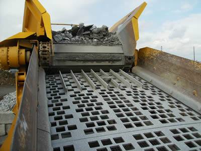 A perforated vibrating screen with square holes and there is a machine on it.