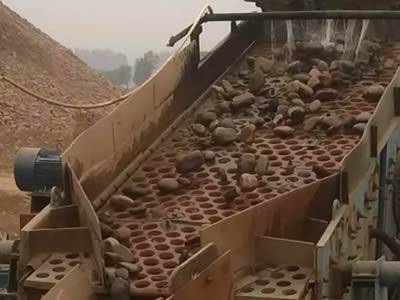A machine with a perforated vibrating screen is screening stones.