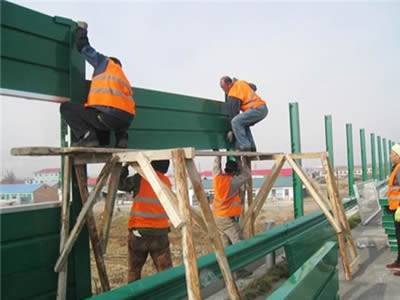 Some people are fixing PVC sound barrier panels in the space between two posts.