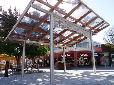In front of the COSTA coffee, there is a perforated sunshade panel supported by four metal posts.