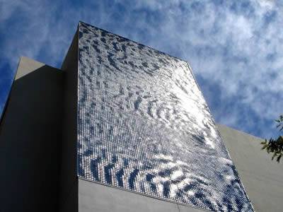 A perforated kinetic facade covered building is under a blue sky.