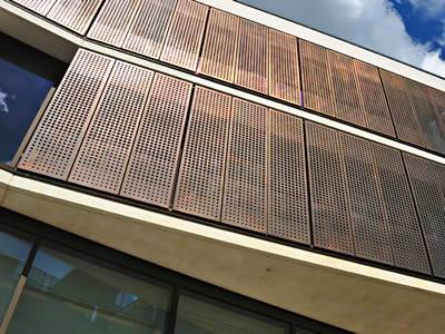 Several orange vertical perforated sunshade panels are for a building wall.